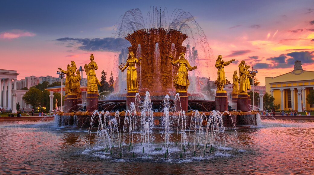 Una fuente con estatua dorada y chorros de agua al atardecer.