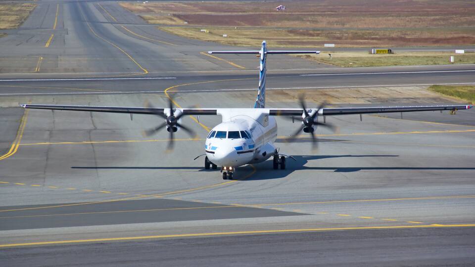 A propeller-driven aircraft on a runway with visible runway markings and distant landscape.