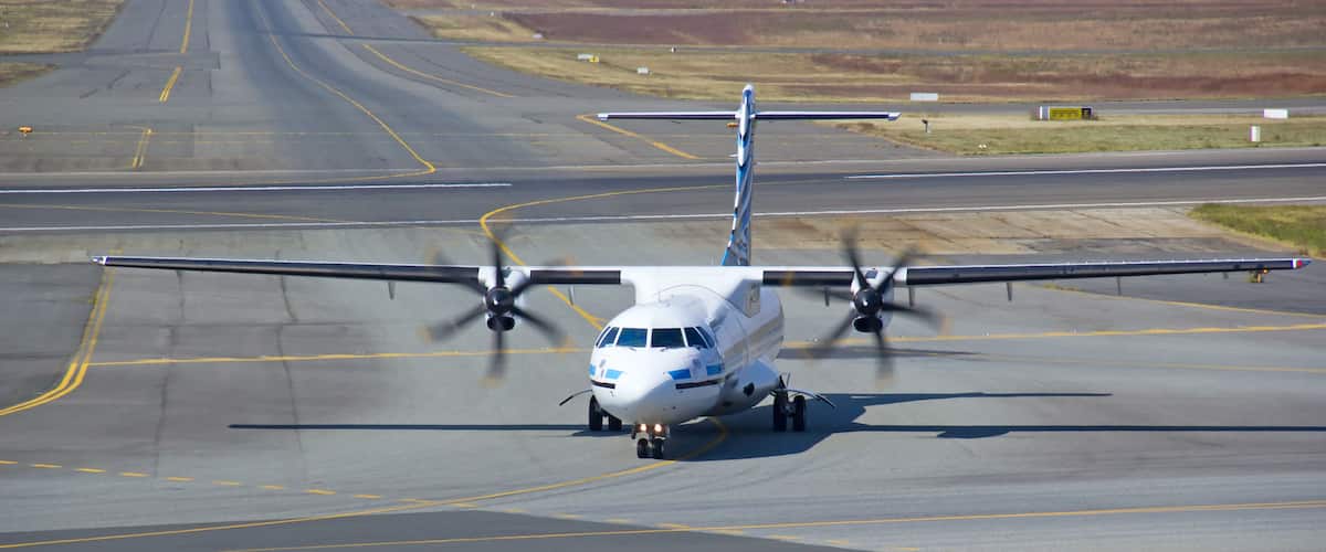 A propeller-driven aircraft on a runway with visible runway markings and distant landscape.
