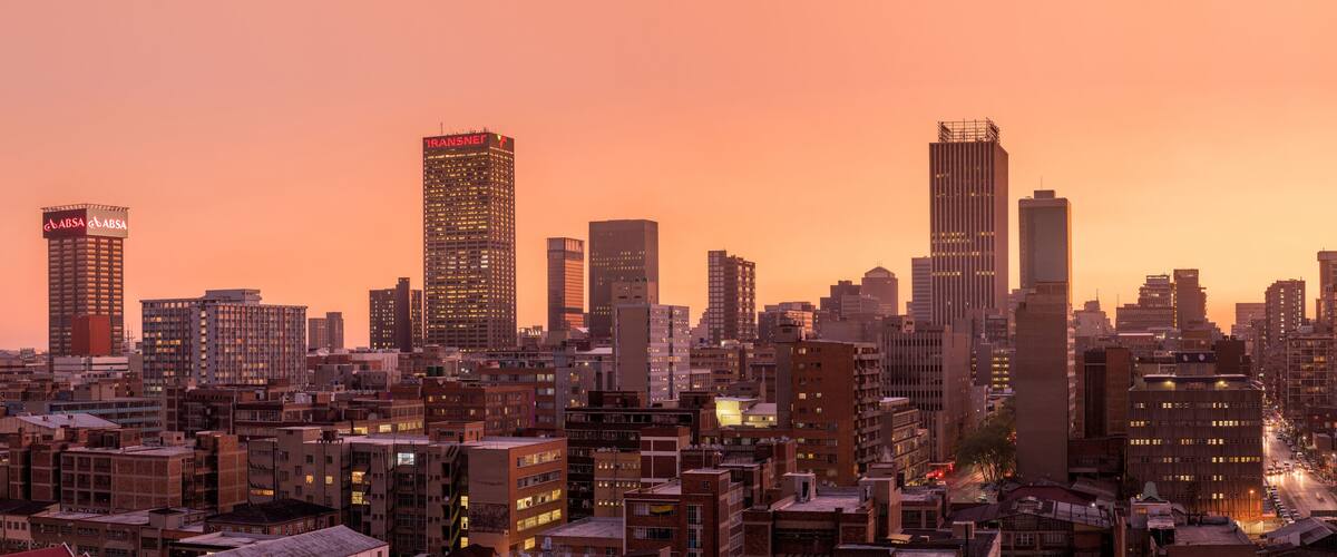 A beautiful and dramatic panoramic photograph of the Johannesburg city skyline, taken on a golden evening after sunset.