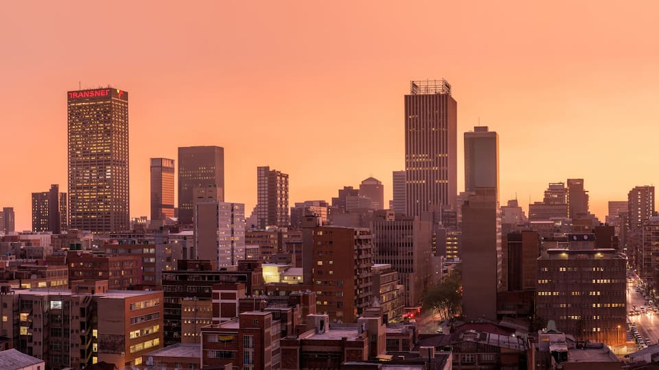 A beautiful and dramatic panoramic photograph of the Johannesburg city skyline, taken on a golden evening after sunset.