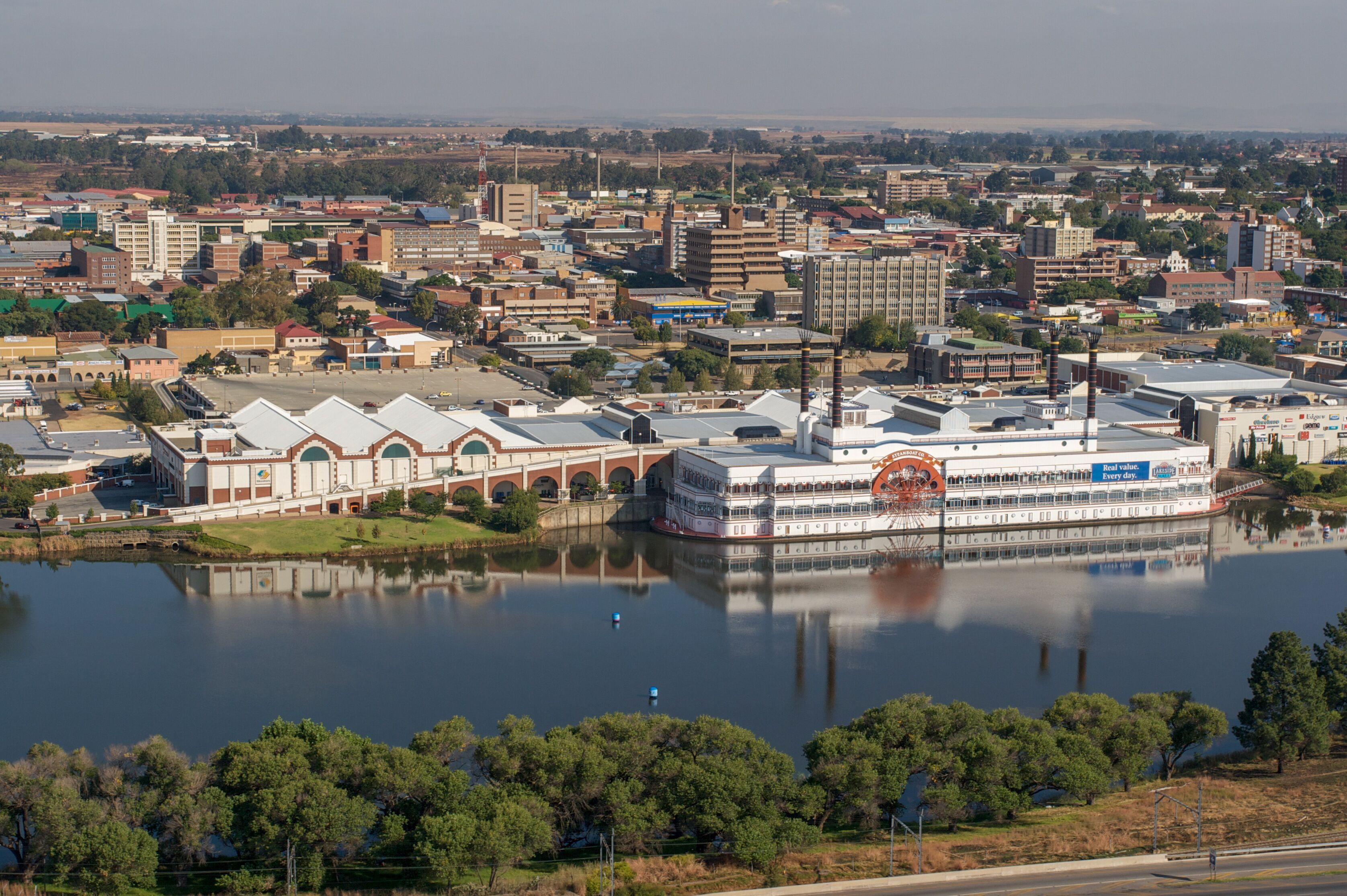 A river with a large boat docked on the right, surrounded by buildings and trees.