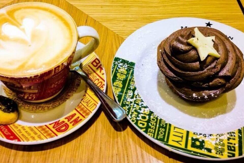 Uma chávena de café com arte de latte, um cupcake de chocolate com uma estrela em cima e um prato com um padrão verde e amarelo.