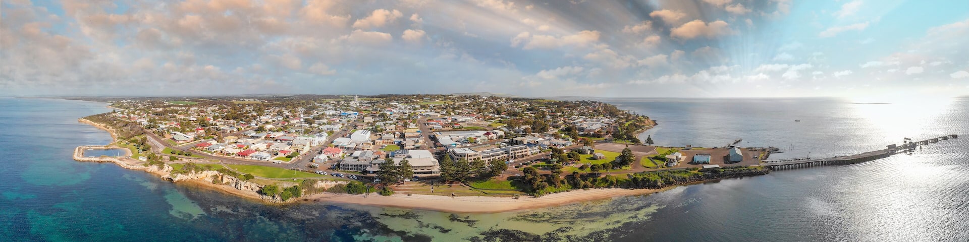 An aerial view of a coastal town with a lighthouse, a pier, and a beach.