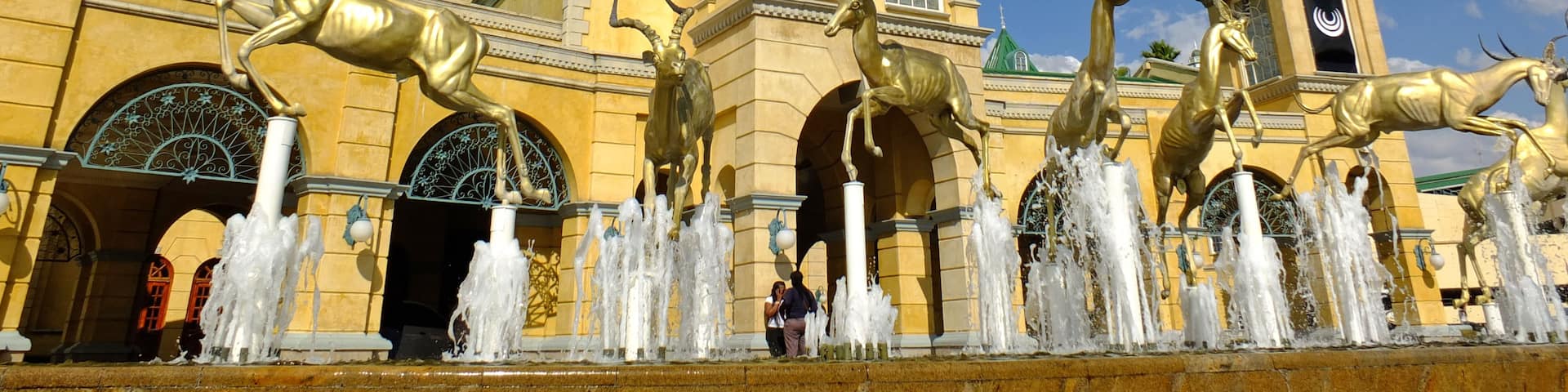 A historic building with a clock tower, ornate windows, and a fountain with golden antelope statues.