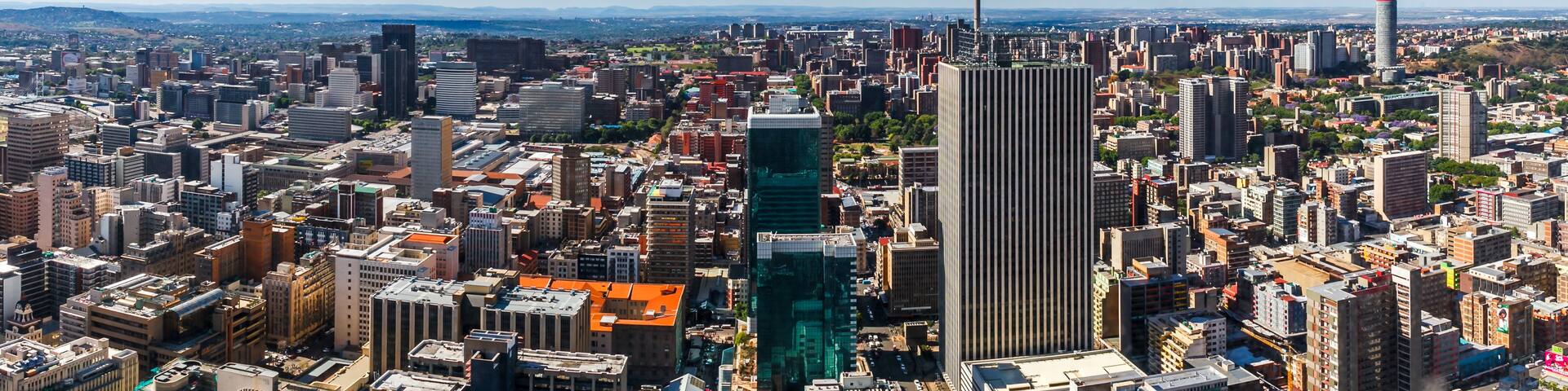 A cityscape with a prominent skyscraper, dense urban buildings, and a clear blue sky.