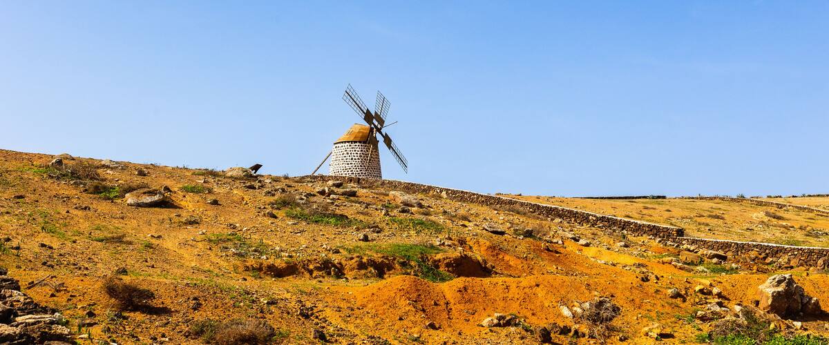 A windmill on a hill with a clear blue sky.