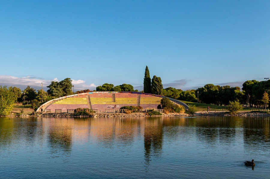 Un gran anfiteatro colorido junto a un lago, con un pato nadando al frente.