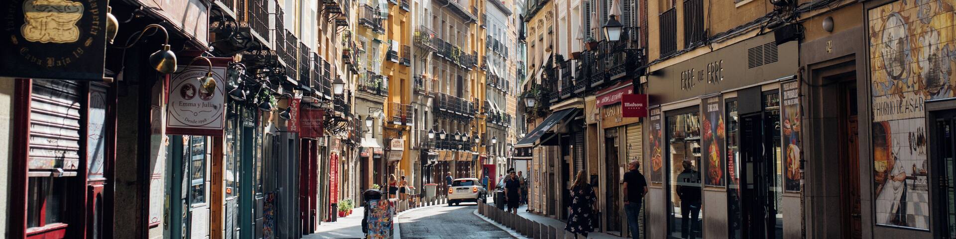 A street with colorful fabric hanging overhead, buildings with balconies, and storefronts.