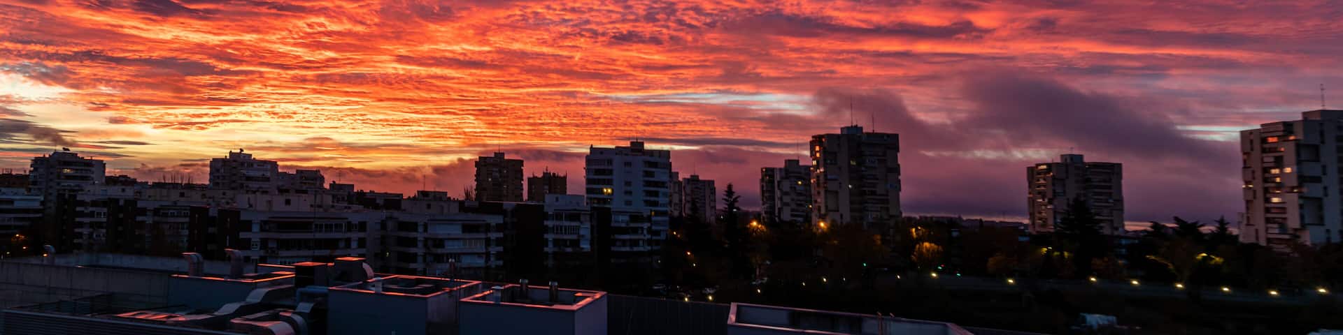A city skyline at sunset with vibrant red and purple clouds.