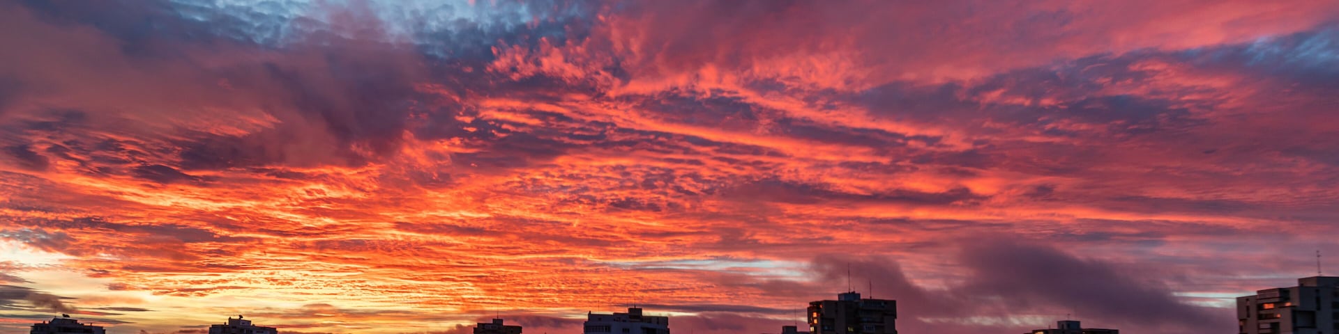 Un horizonte urbano al atardecer con nubes vibrantes de rojo y morado.