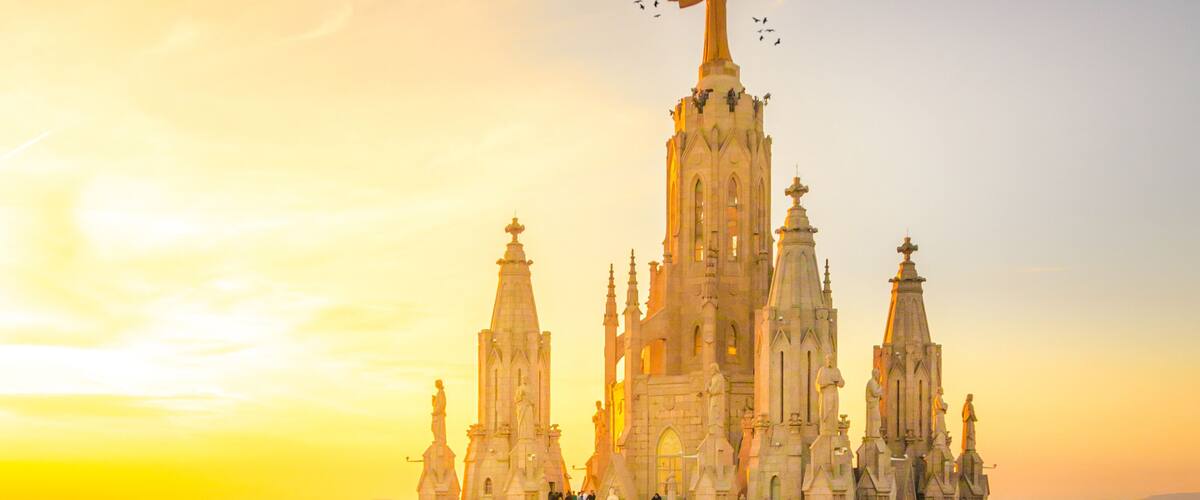 A grand cathedral with intricate architecture, a prominent statue on top, and a surrounding plaza with visitors.