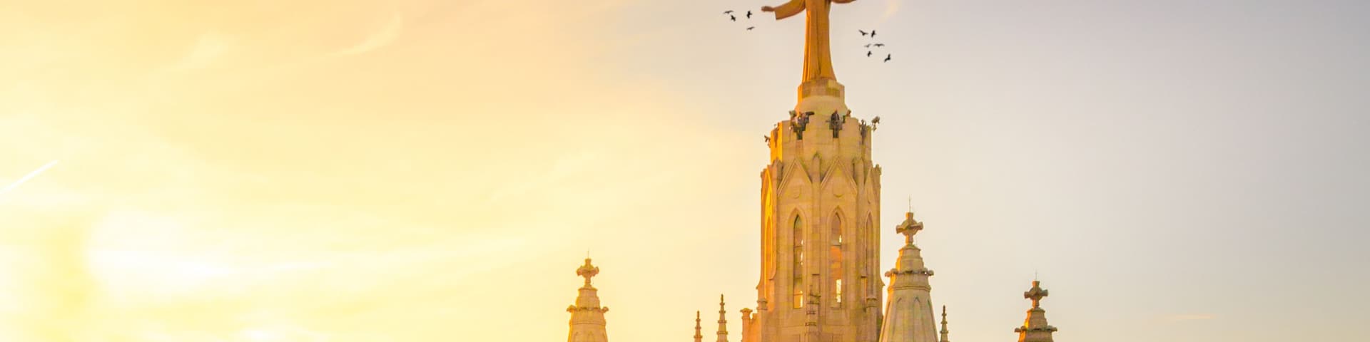 A grand cathedral with intricate architecture, a prominent statue on top, and a surrounding plaza with visitors.