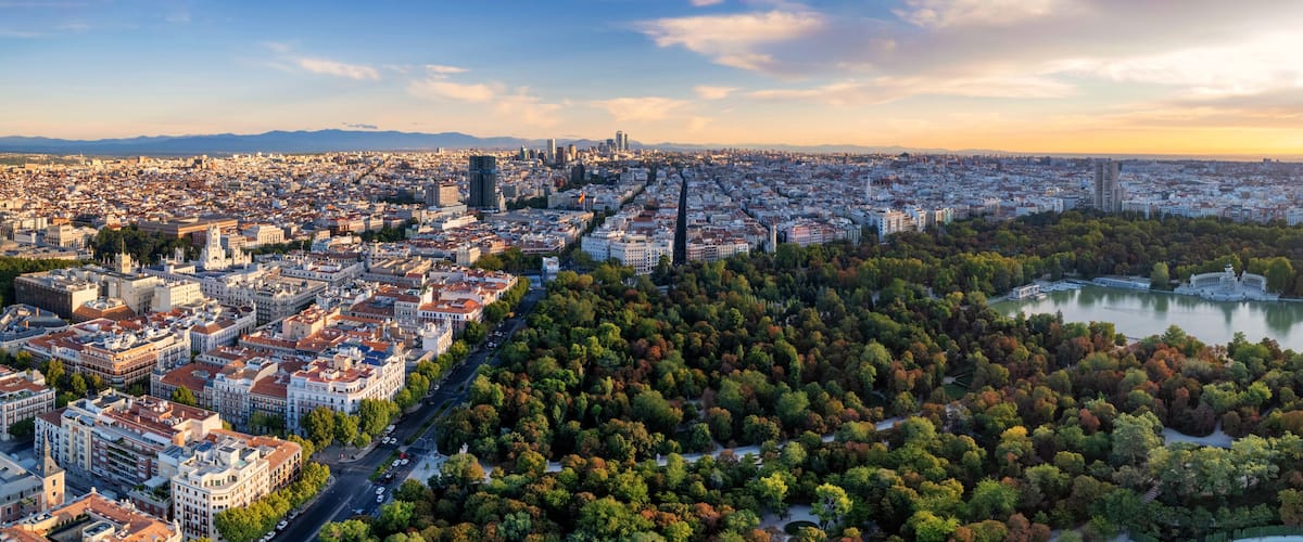 A panoramic view of a city with a dense urban area, a river, and a large park with autumn foliage.