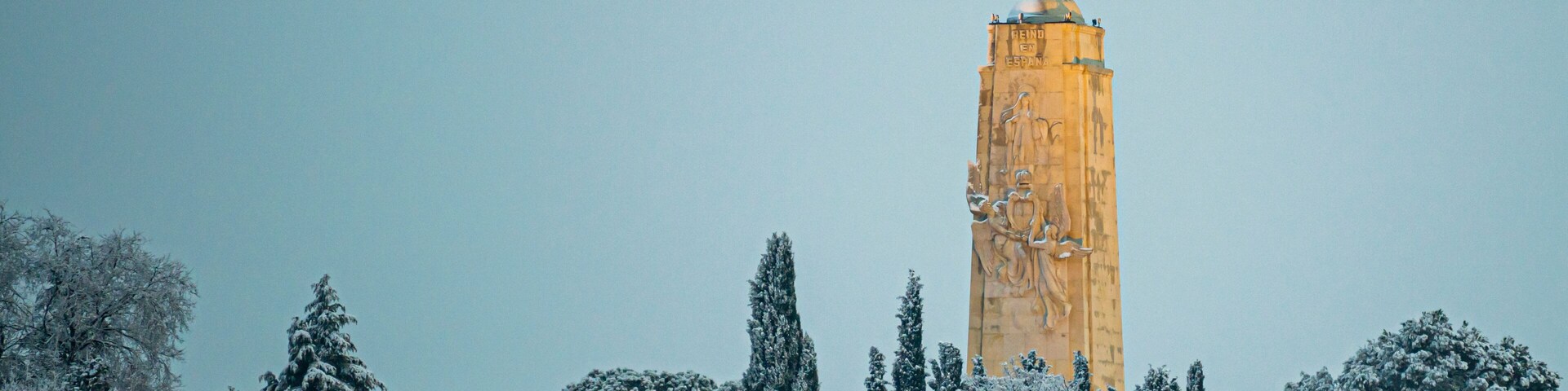 A statue on a tall column with snow-covered trees around it.