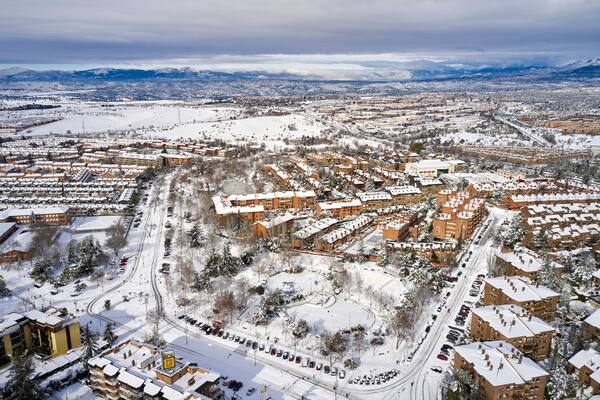 Zona urbana cubierta de nieve con edificios residenciales, calles y montañas al fondo.
