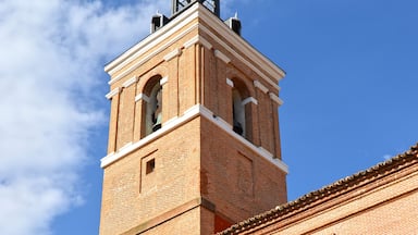 A tall brick tower with a clock and a cross on top, under a clear blue sky.