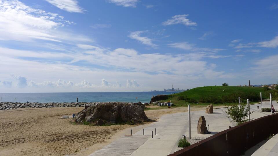 A beach with a wooden walkway, large rocks, and a grassy hill.