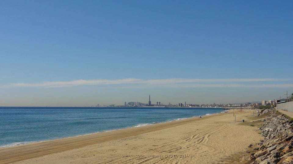 A sandy beach with a rocky shoreline and a city skyline in the distance.