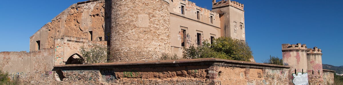 A historic stone tower with a crenellated top, part of a larger ruinous building complex.