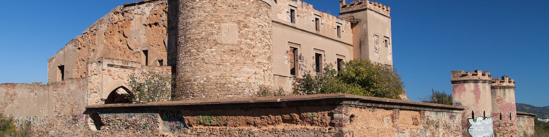 A historic stone tower with a crenellated top, part of a larger ruinous building complex.