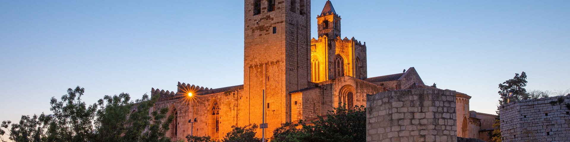 A historic cathedral with a prominent bell tower, surrounded by stone walls and trees.