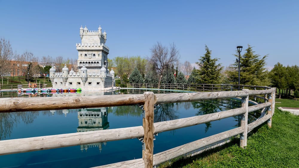 Une structure ressemblant à un château, avec un fossé et une clôture en bois, située dans un parc.