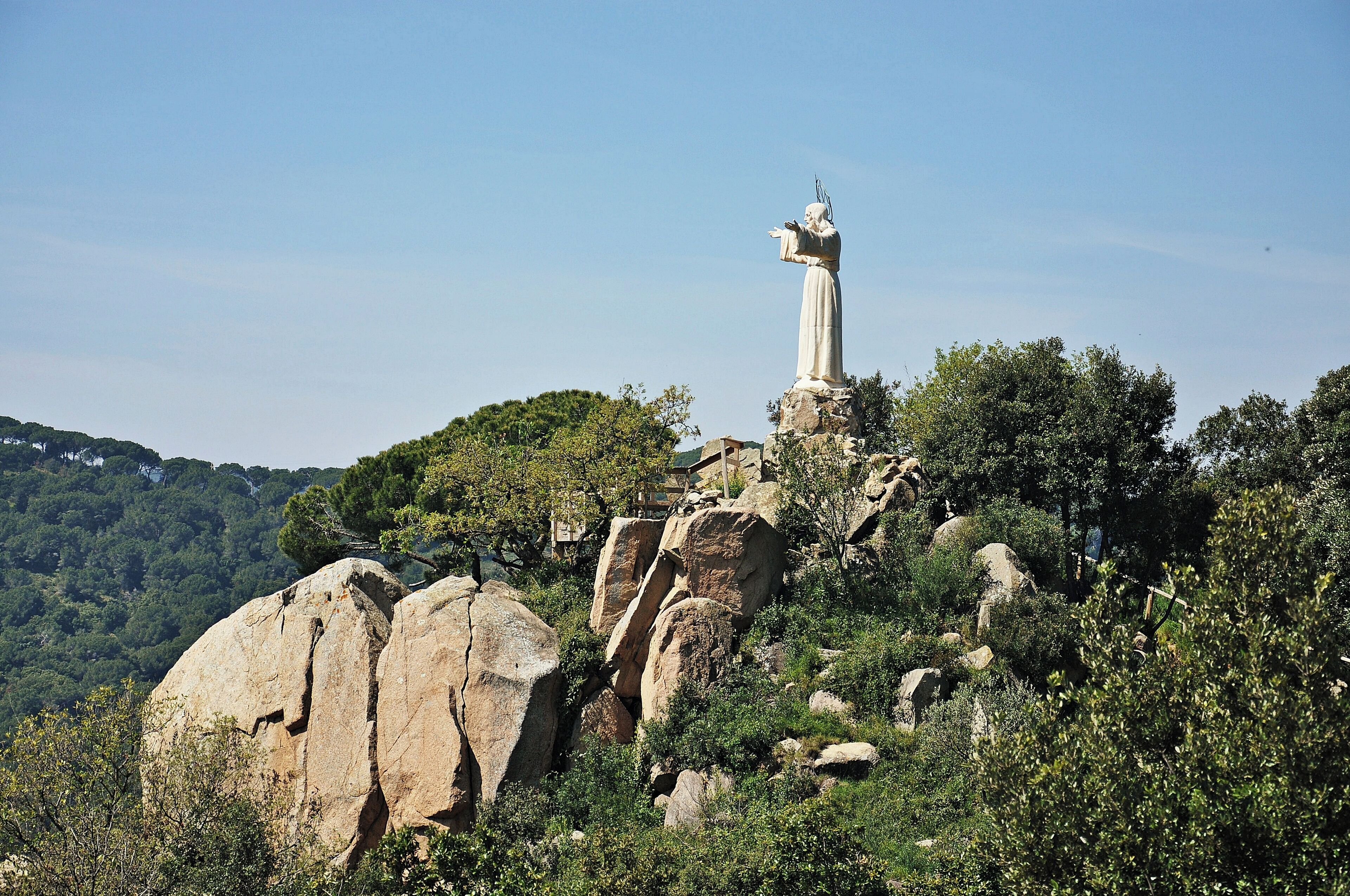 A statue on a rocky outcrop surrounded by trees and hills.