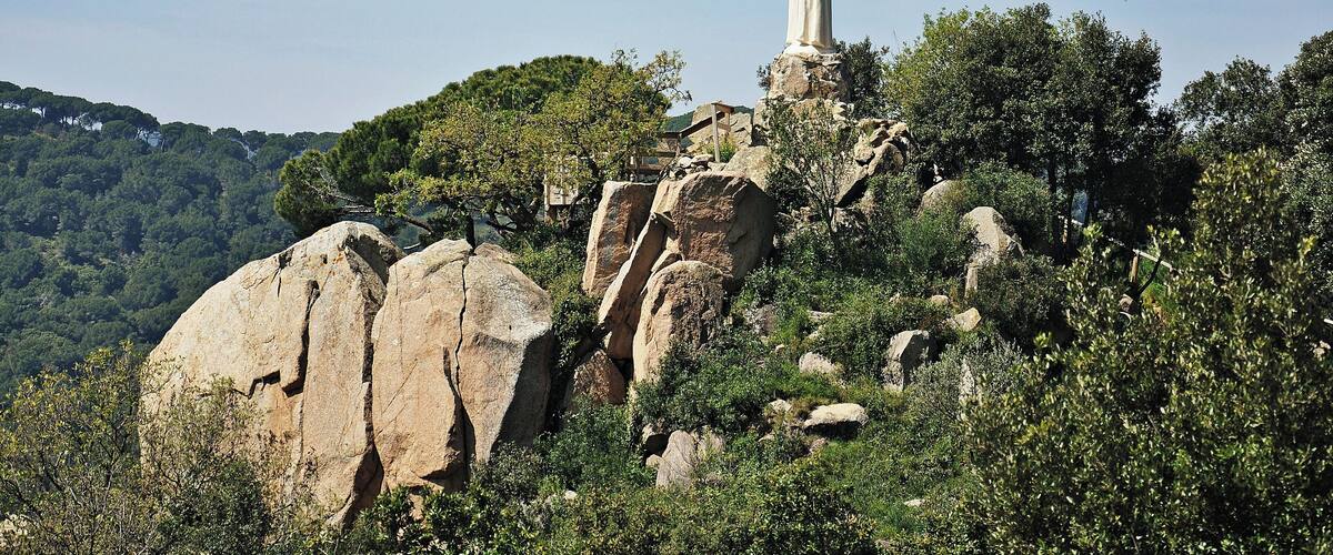 A statue on a rocky outcrop surrounded by trees and hills.