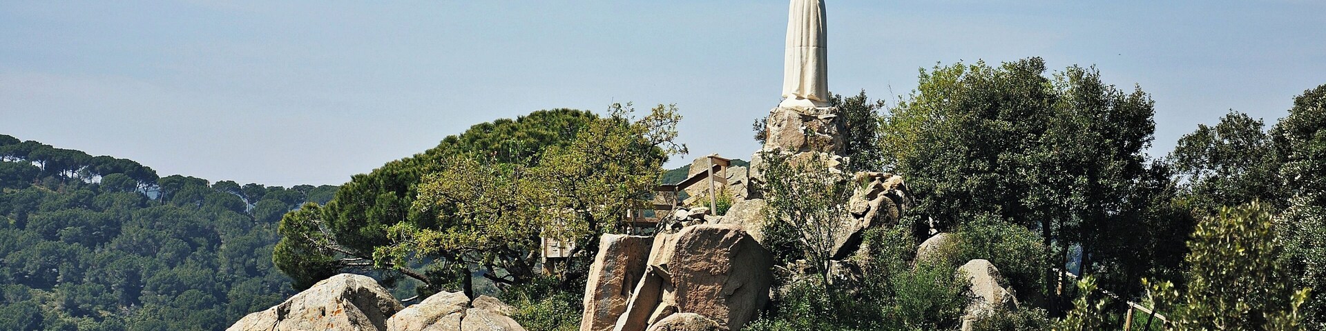 A statue on a rocky outcrop surrounded by trees and hills.