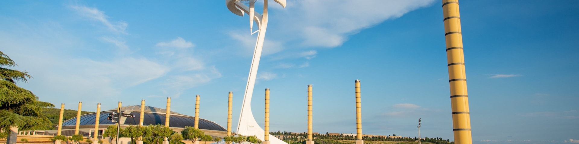 Uma escultura moderna com design espiral branco, cercada por um espelho d'água circular e estruturas cilíndricas altas.