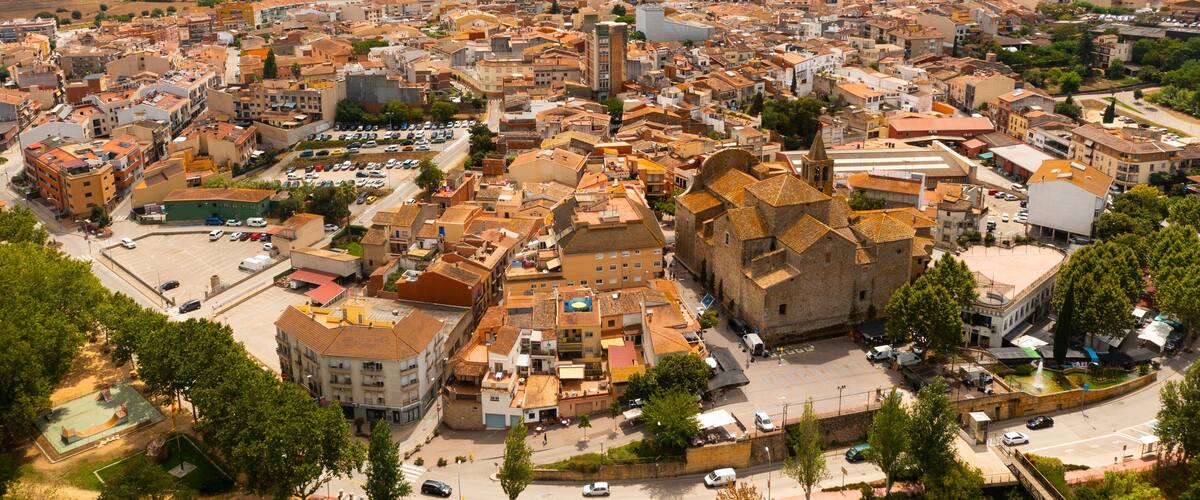 A panoramic view of a historic town with a prominent church, surrounded by lush green hills and a clear sky.