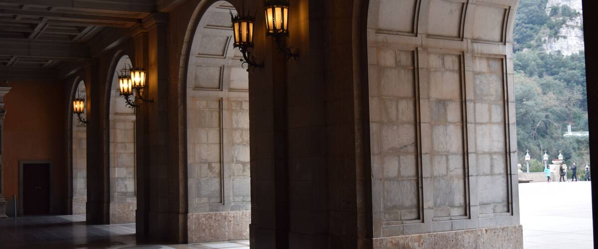 A covered walkway with stone columns and wall-mounted lights.