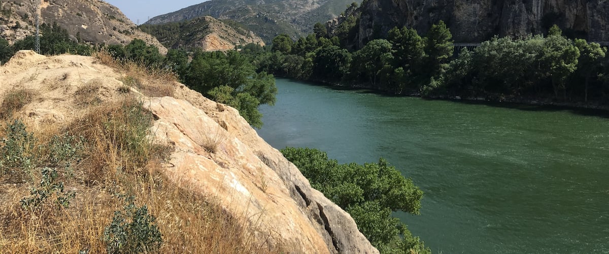 A river flowing through a mountainous landscape with rocky cliffs and dense greenery.