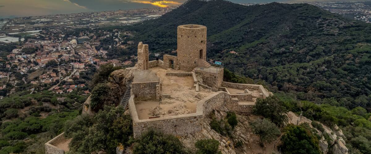 A historic stone fortress overlooking a valley with a sunset in the background.