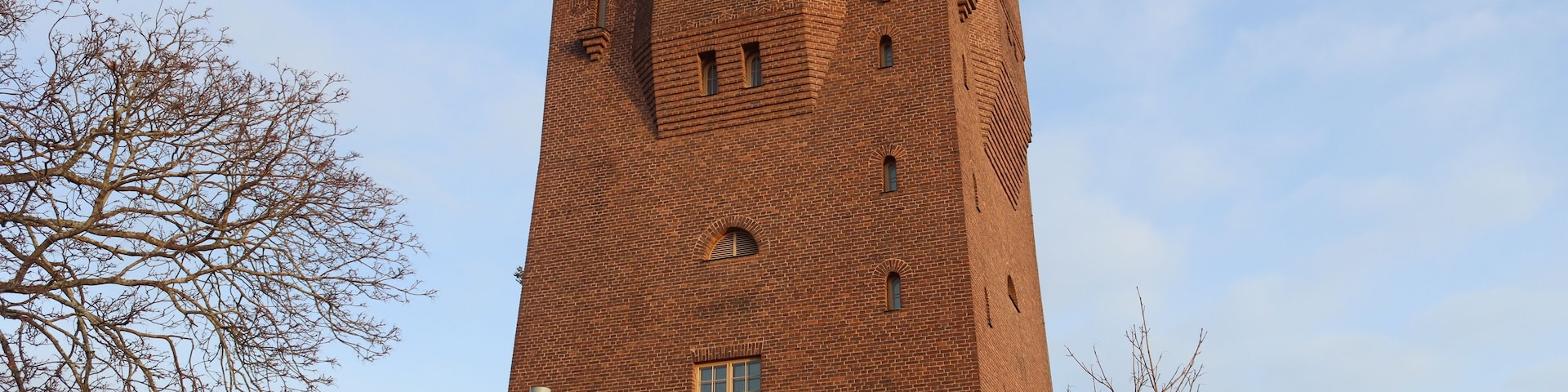 Una alta torre de ladrillo con ventanas de arco y techo plano.