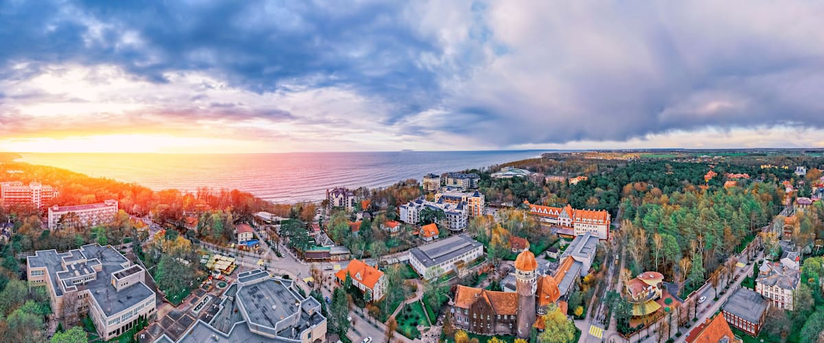 An aerial view of a coastal town with historic buildings, a tower, and a sunset over the sea.