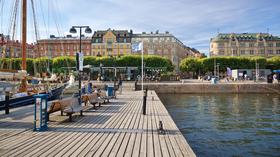 Un muelle de madera con bancos, un bote y un paisaje urbano con edificios históricos al fondo.