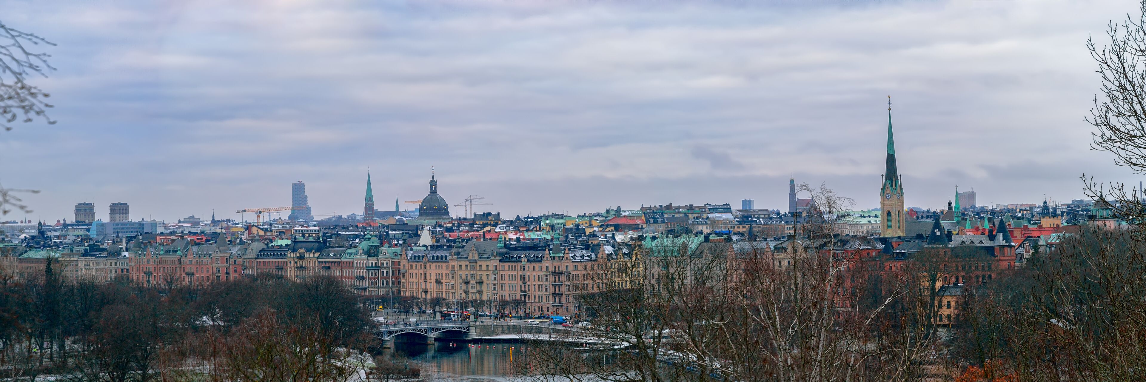 A cityscape with a prominent green spire, a river with bridges, and historic buildings.
