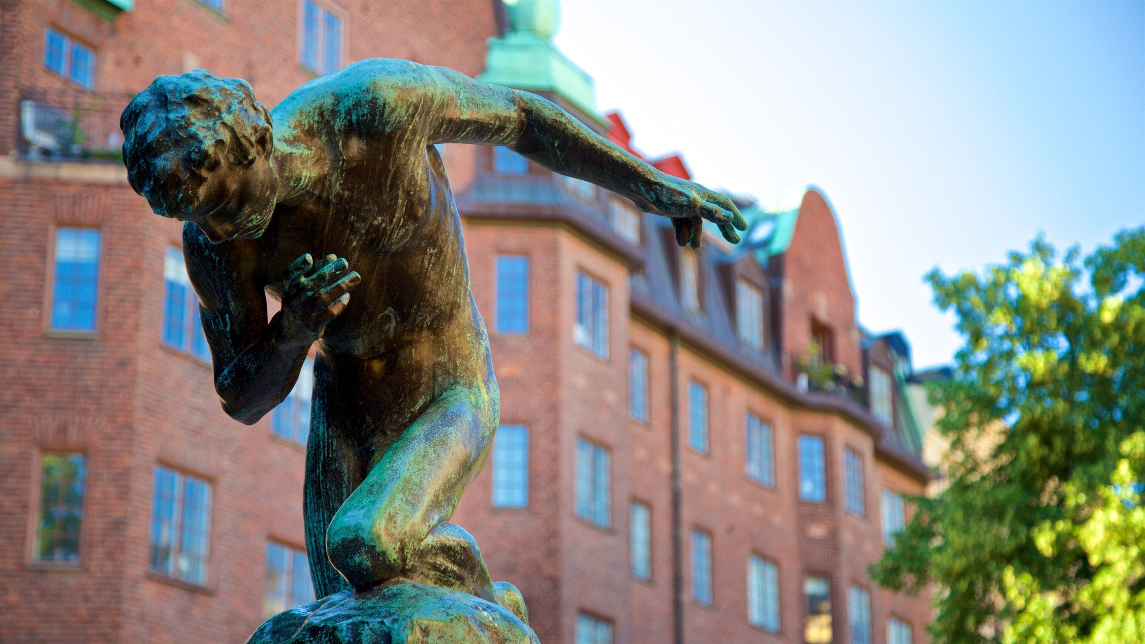 A bronze statue of a man in a dynamic pose, set against a backdrop of a red brick building with multiple windows and a green dome.