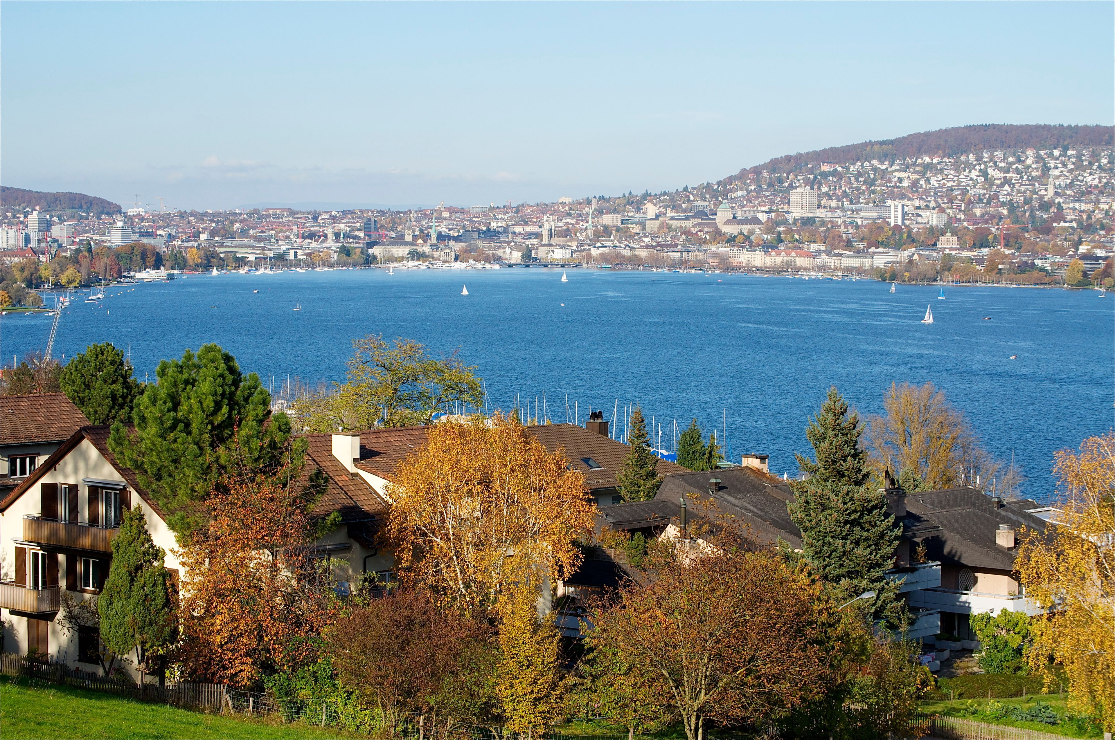 A coastal cityscape with a large body of water, sailboats, and autumn foliage.