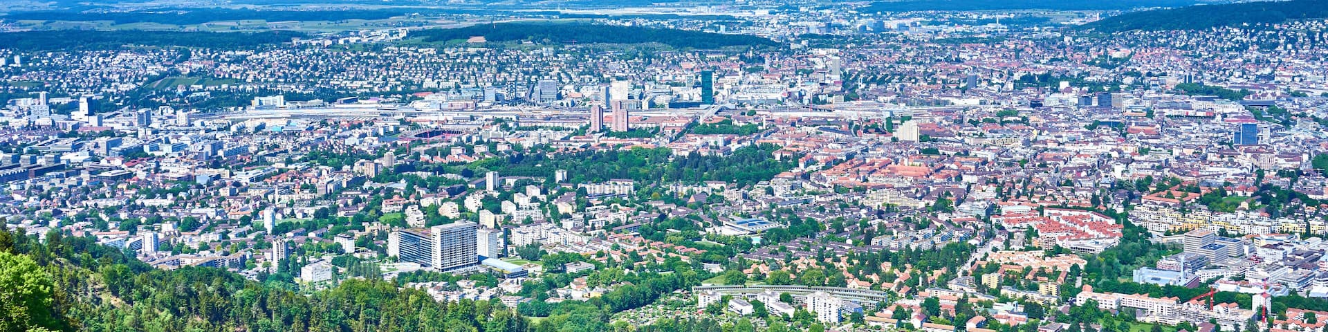 A panoramic view of a city with dense urban areas, green spaces, and distant hills.