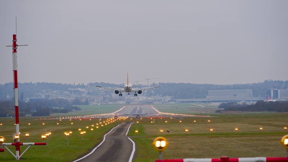 An airplane landing on a runway with airport lights and a distant cityscape.