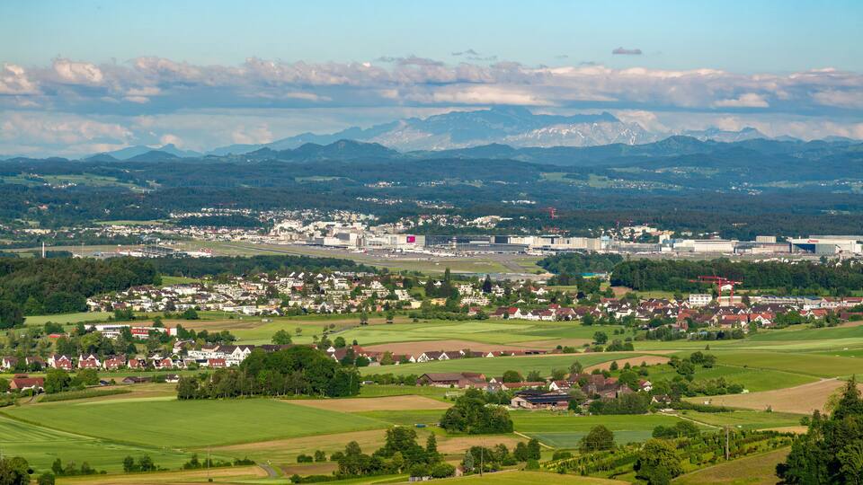 A town with a river, mountains in the background, and green fields.