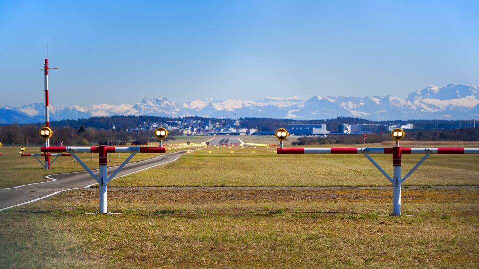 A runway with a control tower, mountains in the background, and a clear sky.