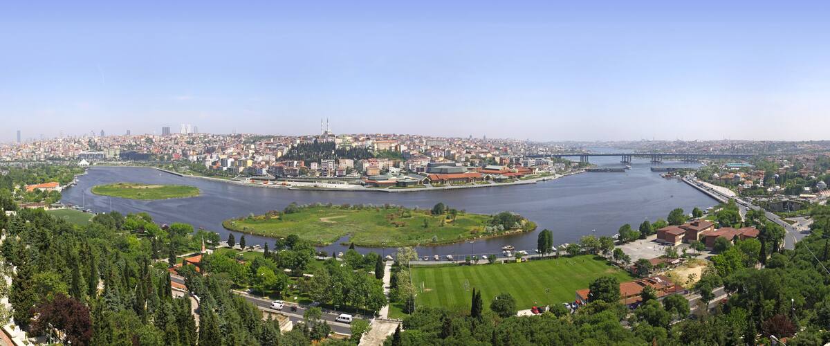 A river flowing through a city with a bridge, green spaces, and historic buildings.