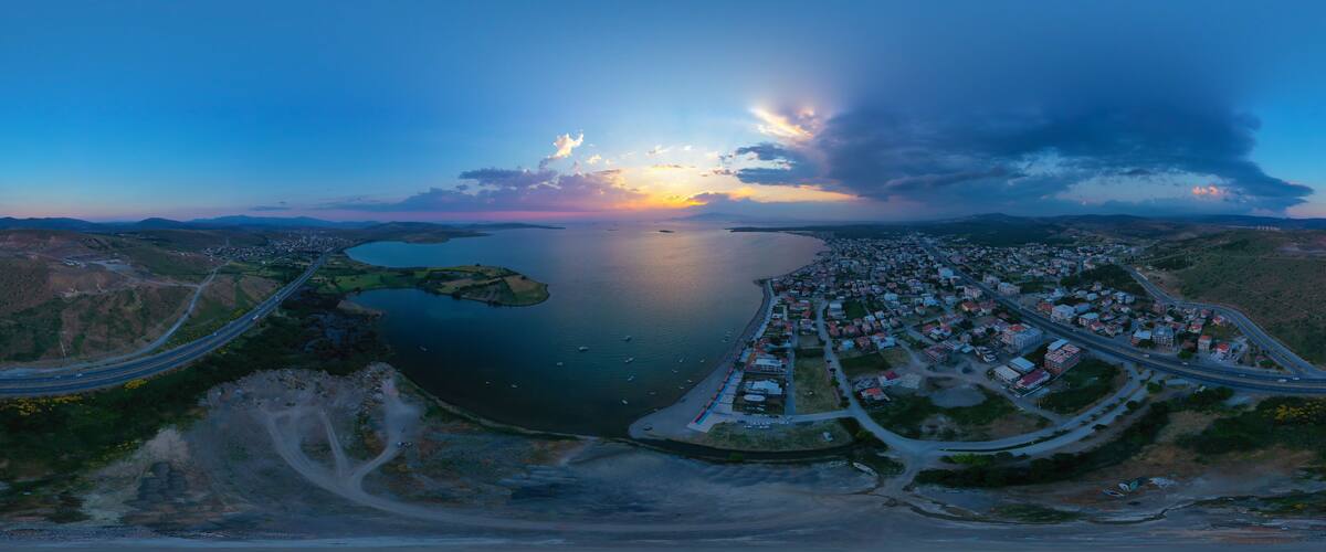 An aerial view of a coastal town with a large body of water, a bridge, and surrounding hills.