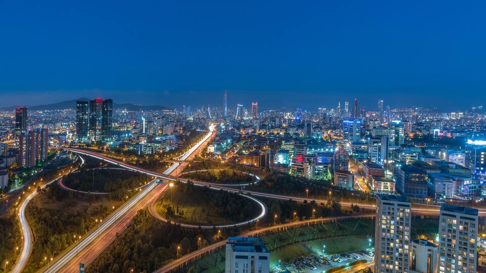 A cityscape at night with illuminated skyscrapers, a curved highway, and a river.