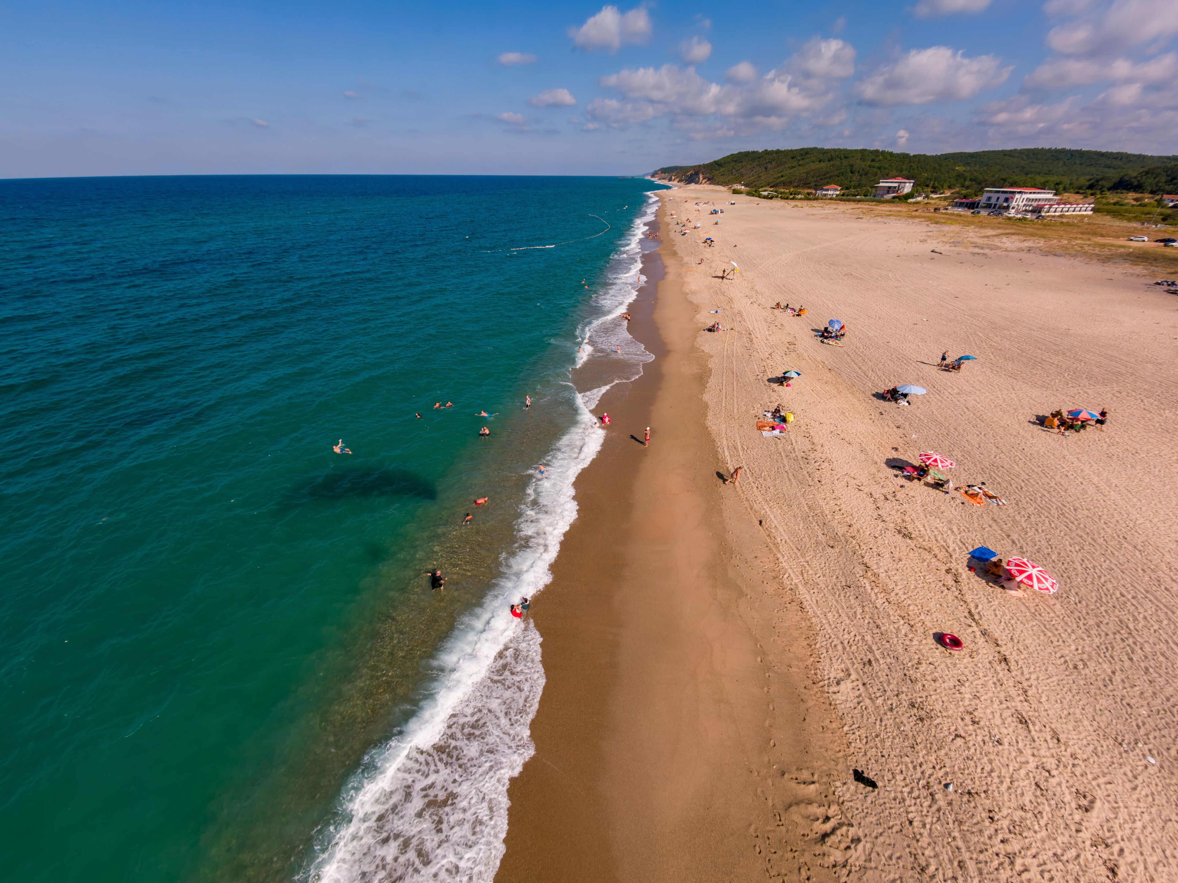 Una amplia playa de arena con agua turquesa cristalina, algunas personas nadando y sombrillas de playa.