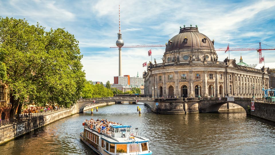 A river with a boat carrying passengers, a bridge, and a large historic building with a dome.